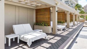 Eine Dachterrasse mit weißen Lounge-Sesseln und Tischen, Holzlamellen und Topfpflanzen.