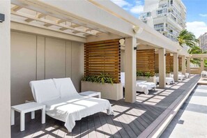 A rooftop lounge area with white lounge chairs and tables, wooden slats, and potted plants. - Newly Renovated Ala Moana with Balcony (Honolulu)
