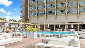 A hotel with a rooftop pool area, lounge chairs, and a large building with balconies.