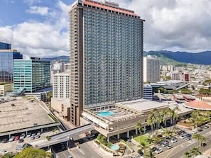 Ein Hochhaus-Hotel mit Pool, Parkplätzen und Blick auf Stadt und Berge.