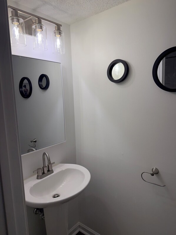 Une salle de bain avec un lavabo blanc, un miroir et trois lampes suspendues.