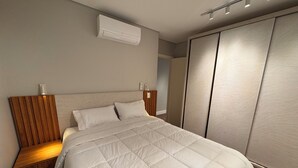 A modern bedroom with a large bed, wooden headboard, bedside tables with lamps, an air conditioning unit, and a sliding wardrobe.