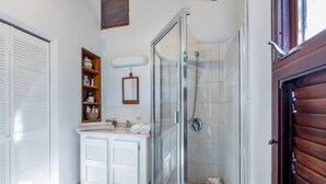 Een badkamer met een douchecabine van glas, een wit wastafelmeubel met een spiegel, en een houten plank met toiletartikelen.