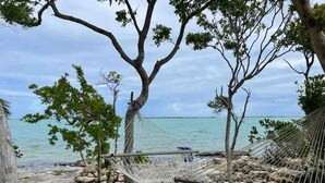Een hangmat tussen bomen, een rotsachtig strand en een rustige zee.