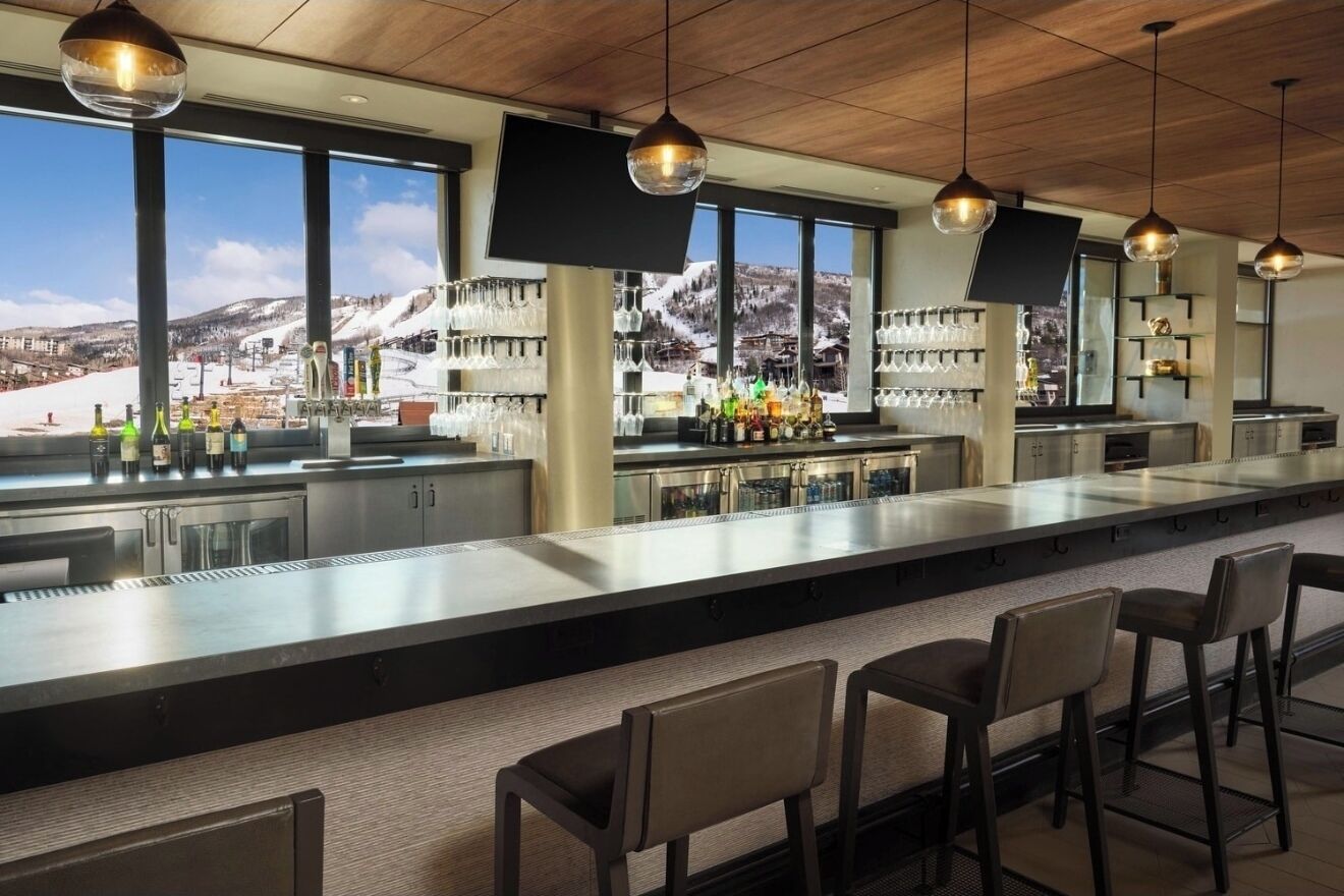 Un espace bar doté d’un long comptoir, de tabourets de bar et offrant une vue sur un paysage montagneux enneigé grâce à de grandes fenêtres.