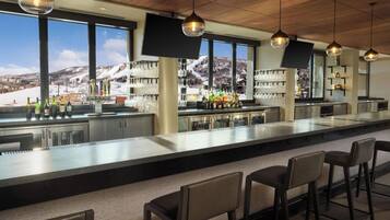 Un espace bar doté d’un long comptoir, de tabourets de bar et offrant une vue sur un paysage montagneux enneigé grâce à de grandes fenêtres.