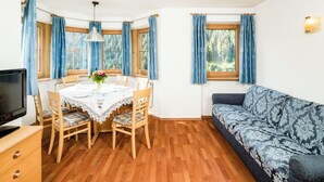 A room with a dining table set for four, a sofa, a television, and a window with curtains. - Apartments Hetty (Santa Cristina Valgardena)