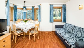 A room with a dining table set for four, a sofa, a television, and a window with curtains. - Apartments Hetty (Santa Cristina Valgardena)