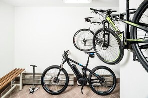 A room with a bicycle rack holding two bicycles, a bench, and a scooter. - Apartments Hetty (Santa Cristina Valgardena)