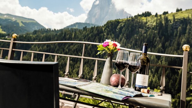 A table with a bottle of wine, two glasses, a vase with flowers, and a map. - Apartments Hetty (Santa Cristina Valgardena)