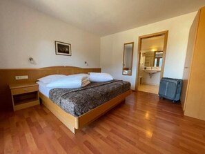 Ein Schlafzimmer mit einem hölzernen Bett, einem Nachttisch, einem Spiegel und einem Koffer.