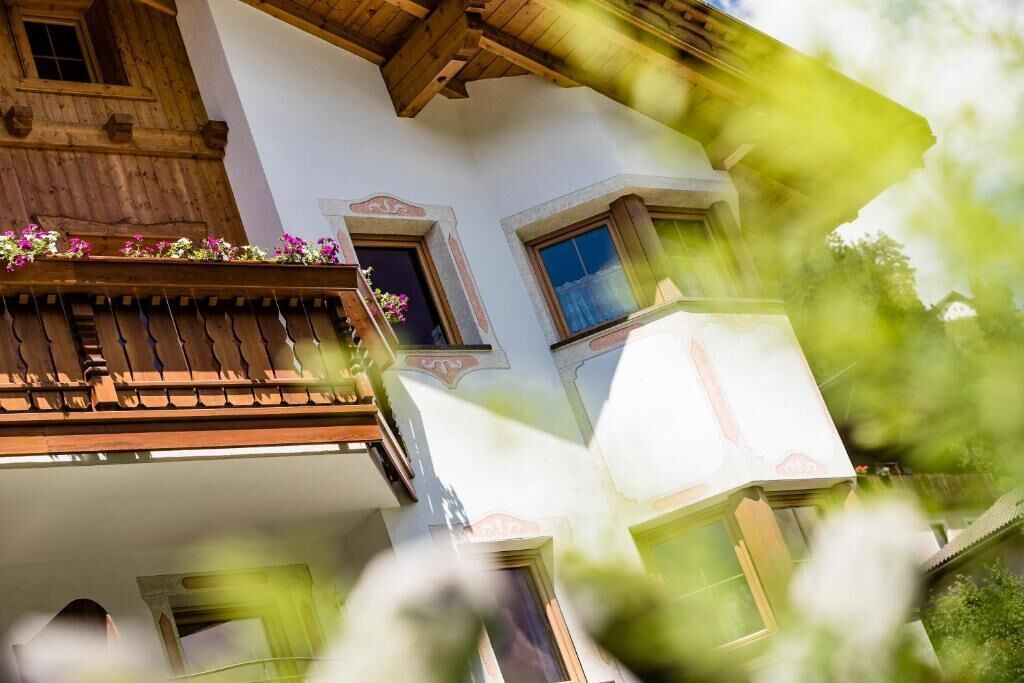 Ein mehrgeschossiges Gebäude mit einem Holzbalkon, einem Fenster mit Blumenkasten und einem Balkon mit Geländer.