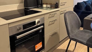 A compact kitchen with a built-in oven, a coffee maker, and a small countertop. - Cozy Botanical Gardens Apartment | Sleeps 5 Guests 🌿 (Stretford)
