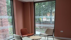 A modern interior with two chairs and a small table, large windows with a view of a fence and trees, and a brick wall. - Cozy Botanical Gardens Apartment | Sleeps 5 Guests 🌿 (Stretford)