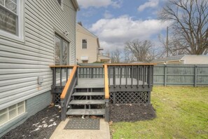 Eine Holzterrasse mit Geländer, die zu einem Haus mit grauer Fassade führt.