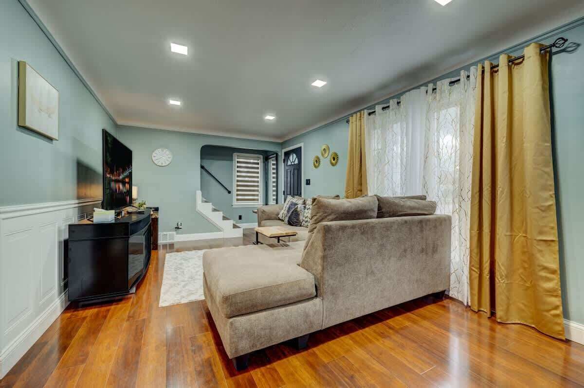 Sunlit living space w/ large windows, soft curtains & relaxed seating