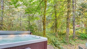 A hot tub in a forested area with a wooden bench and a rock nearby. - Large log home in Lake Lure, HOT tub/Game room/pet (Lake Lure)