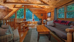 A cabin interior with a wooden ceiling, large windows, a sofa, a table, and a chair. - Large log home in Lake Lure, HOT tub/Game room/pet (Lake Lure)