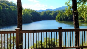 A wooden deck overlooking a calm lake surrounded by dense forest and mountains.