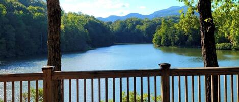 Una terraza de madera con vistas a un lago tranquilo rodeado de bosque denso y montañas.