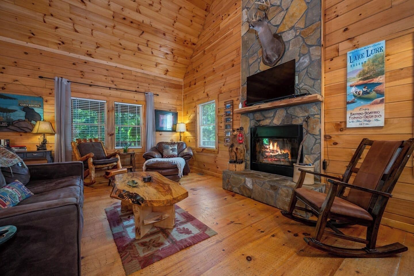 A log cabin interior with a fireplace, leather furniture, and a mounted deer head.