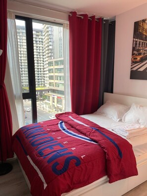 A hotel room with a bed, a window with curtains, and a view of buildings outside. - CONDO DOWNTOWN MONTREAL - GRIFFINTOWN W (Montréal)