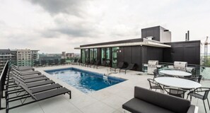 A rooftop pool area with lounge chairs, a barbecue grill, and a glass-enclosed building. - CONDO DOWNTOWN MONTREAL - GRIFFINTOWN W (Montréal)
