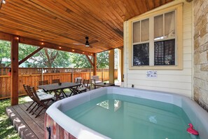 A covered outdoor area with a hot tub, wooden deck, and a window overlooking a backyard.