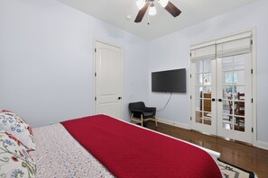 A bedroom with a bed, a TV mounted on the wall, and a ceiling fan.