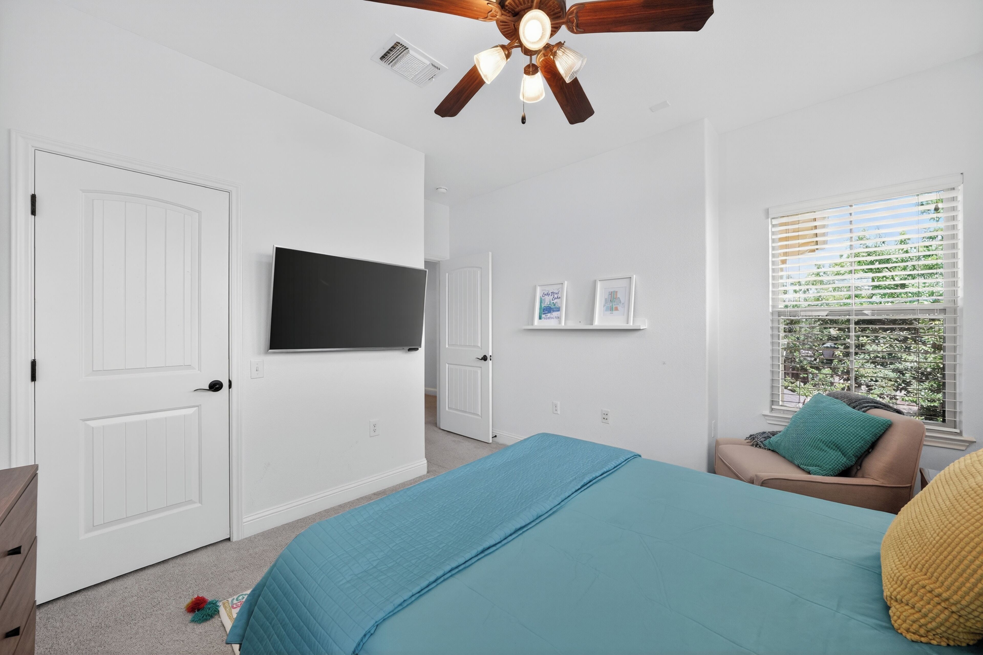 Une chambre à coucher avec un lit, un ventilateur de plafond, une télévision, une fenêtre avec des stores et une porte.