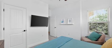 Une chambre à coucher avec un lit, un ventilateur de plafond, une télévision, une fenêtre avec des stores et une porte.