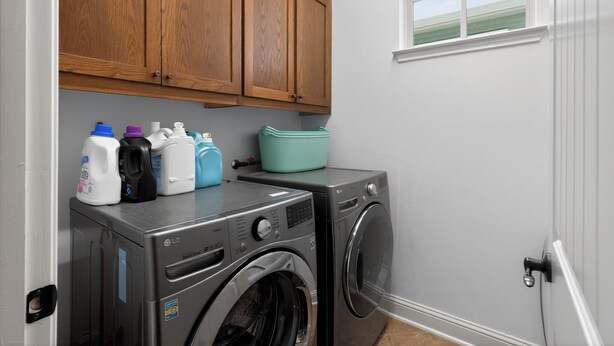 Un espace buanderie équipé d’un lave-linge et d’un sèche-linge, avec des placards en bois au-dessus et une fenêtre offrant une vue agréable.