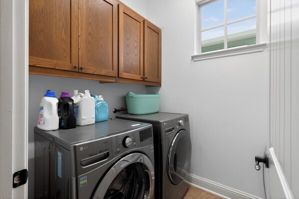 A laundry area with a washing machine and dryer, wooden cabinets above, and a window with a view.