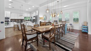 A spacious kitchen with modern appliances, a dining area with wooden chairs and a large table, and a view of the outdoors through large windows.