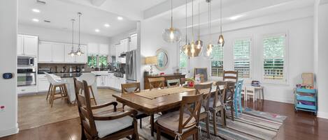 A spacious kitchen with modern appliances, a dining area with wooden chairs and a large table, and a view of the outdoors through large windows.