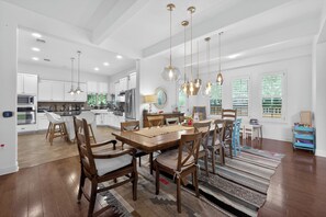 A spacious kitchen with modern appliances, a dining area with wooden chairs and a large table, and a view of the outdoors through large windows.