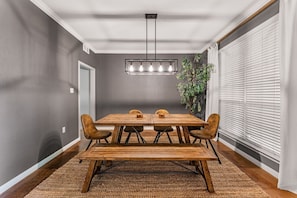 A dining area with a wooden table, four chairs, a hanging light fixture, and a plant. - Pet-Friendly Near Baylor & Magnolia|HotTub+Firepit (Waco)