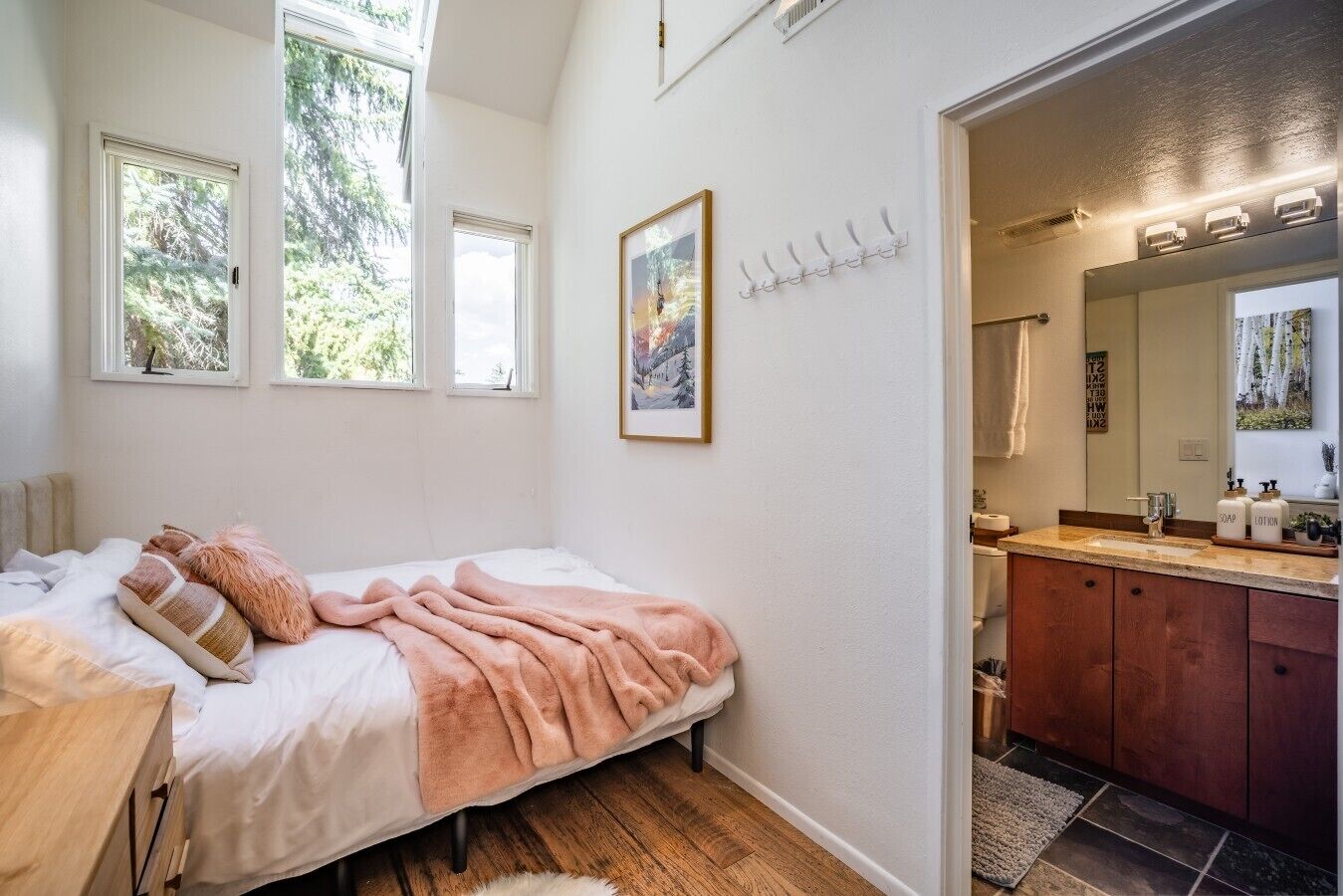Une chambre à coucher comprenant un lit, une table de chevet, une fenêtre et une porte donnant sur une salle de bain.
