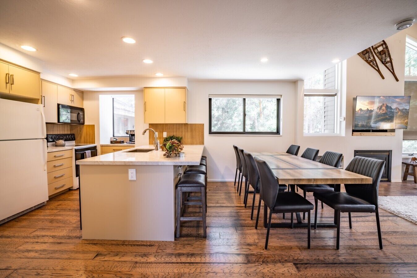 Una cocina moderna con una isla central, zona de comedor con una mesa larga y sillas, y ventanas amplias que ofrecen luz natural.