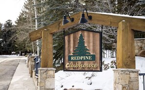Ein hölzernes Schild mit dem Logo eines Kiefernbaums und dem Text 'REDPINE Clubhouse', das eine Lodge oder einen Rückzugsort kennzeichnet.