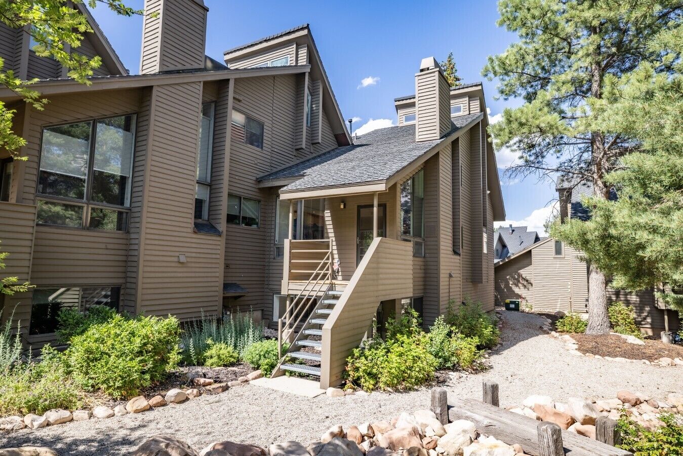 A modern two-story house with a prominent staircase leading to the entrance, surrounded by a landscaped garden with various shrubs and a gravel path.
