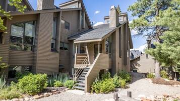 A modern two-story house with a prominent staircase leading to the entrance, surrounded by a landscaped garden with various shrubs and a gravel path.