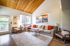 Ein geräumiges Wohnzimmer mit hoher Decke, großen Fenstern, einer Sofagarnitur und einem Couchtisch.