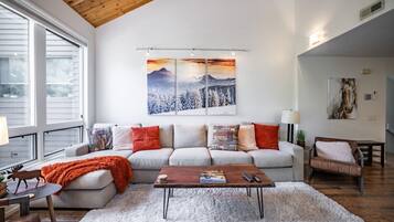 Een moderne woonkamer met een hoge plafond, een zithoek, een salontafel en kunstwerken aan de muur.