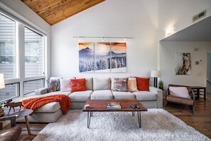 A modern living room with a high ceiling, a sofa set, a coffee table, and artwork on the wall. - Park City Canyons Ski Chalet | Heated Pool/Hot Tub, Shuttle, 30- sec walk to Gondola (Park City)