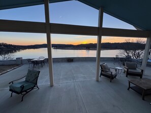 Eine überdachte Terrasse mit Gartenmöbeln, Blick auf einen See und ein Sonnenuntergang.