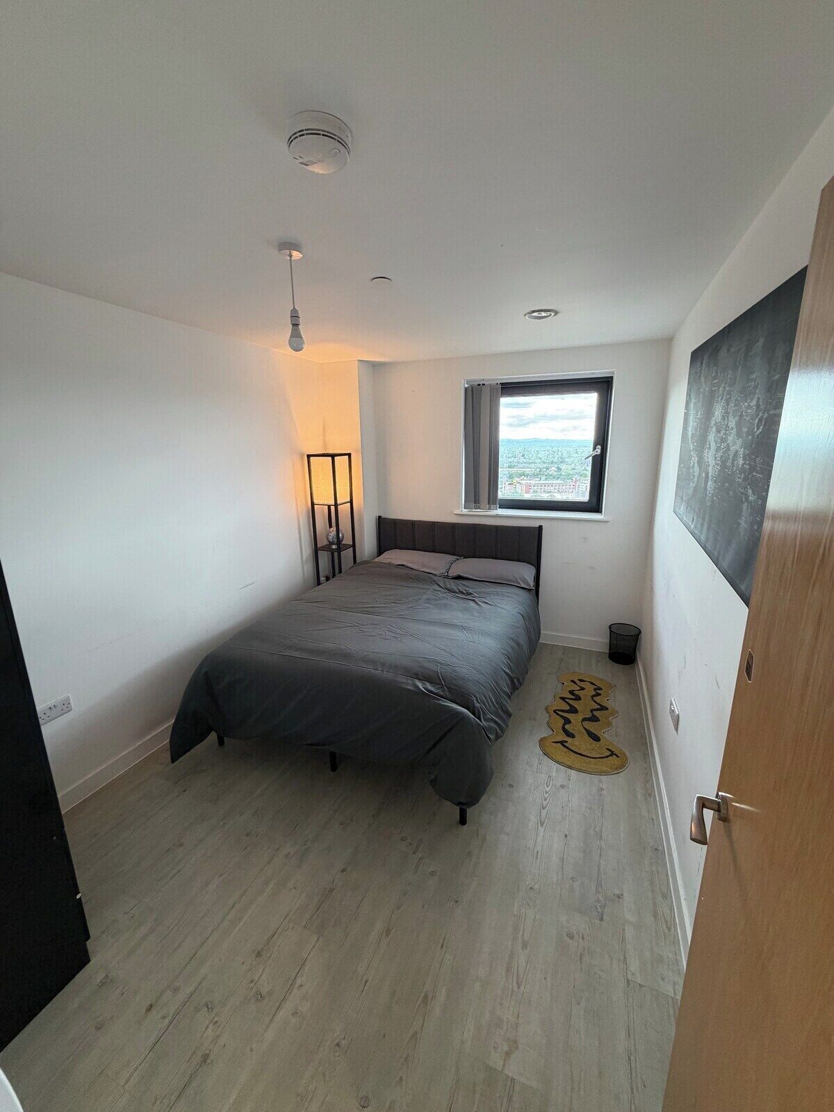 Une chambre à coucher avec un lit, une fenêtre donnant sur un paysage agréable, une lampe et une porte.