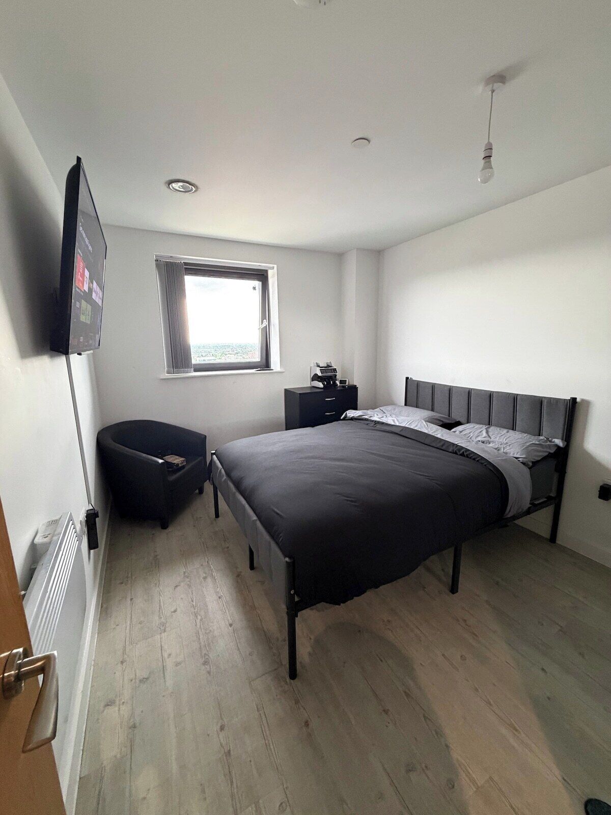 A bedroom with a bed, a window, a desk, and a flat-screen TV mounted on the wall.