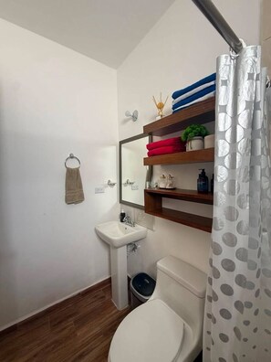 A bathroom with a toilet, sink, and a mirror above it. There are shelves with towels and toiletries. - Casa Bambu, Playa del Carmen. (Playa del Carmen)