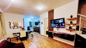 Uma sala de estar moderna com televisão de tela plana, piso de madeira e um espaço de jantar com mesa e cadeiras.